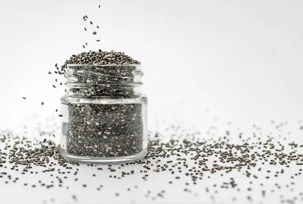 Wlewanie suchych nasion chia do szklanego słoika na białym tle. Odizolowane, kopiuj przestrzeń. Chia superfood paleo koncepcja diety. — Zdjęcie stockowe