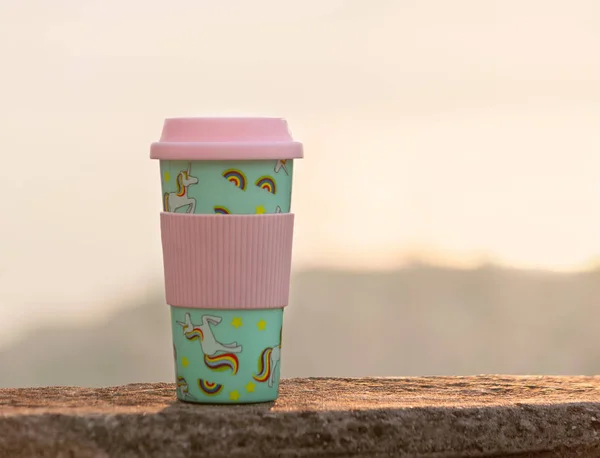 Reusable plastic travel mug tumbler decorated with an all-over print of rainbow coloured unicorn on pastel green background.