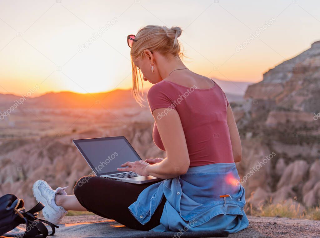 Young woman sitting outdors with laptop during sunset. 
