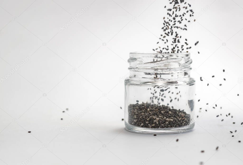 Pouring dry chia seeds into glass jar on white background. Isolated, copy space. Chia superfood paleo diet concept.