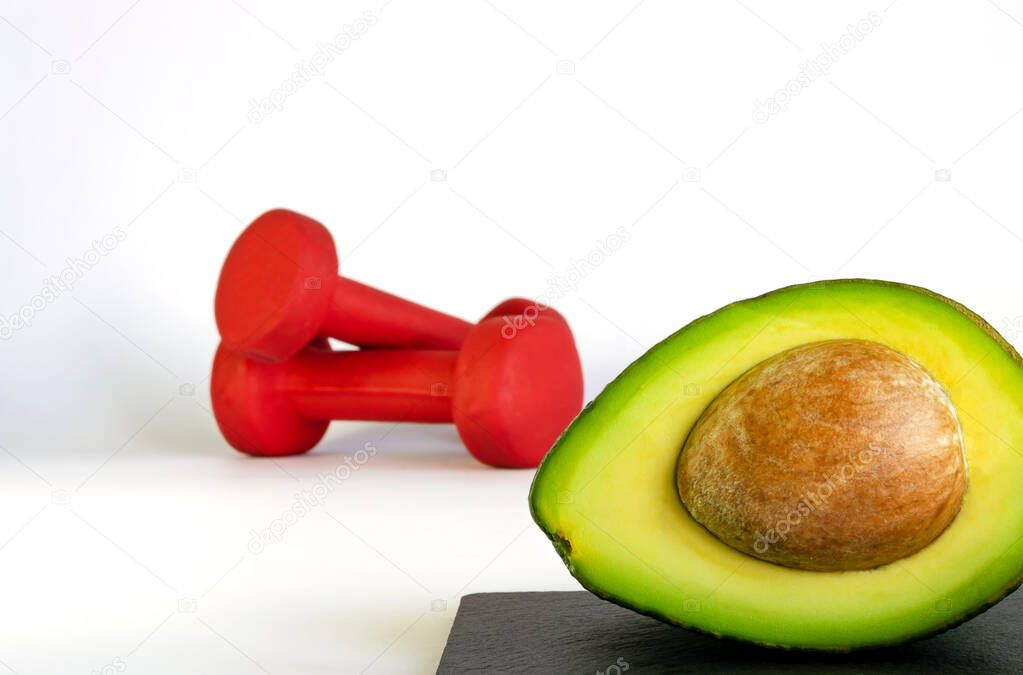 Fresh avocado with unfocused red dumbbells on background. Concept of healthy eating and sports. 