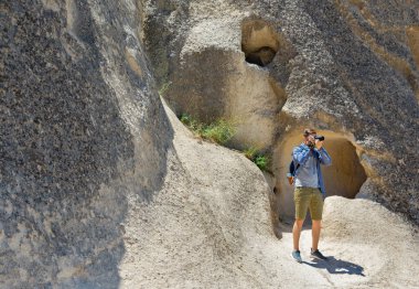 Genç fotoğrafçı dağlarda yürüyor, profesyonel kamerayla fotoğraf çekiyor..