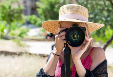 Hasır şapkalı kadın fotoğrafçı ve DSR profesyonel kamera açık havada çekim yapıyor..