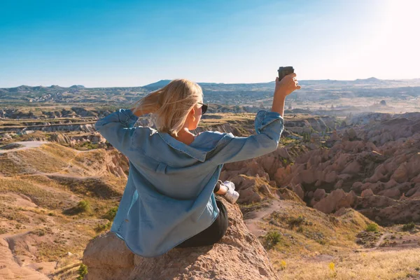 Back view of woman with tumbler cup of coffee sitting on the hill enjoying scenery.