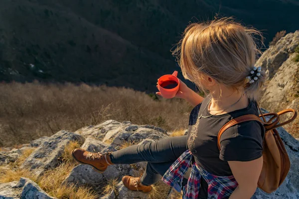 崖の端にあるコーヒーを飲みながらリラックスした若い女性ハイカーは 美しい山々の景色と日没を楽しんでいます 頭上からの眺めコピースペースハイキング旅行のコンセプト — ストック写真