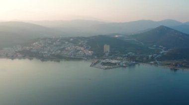 Gün batımında arka planda deniz, rıhtım ve dağların üzerinde uçan insansız hava aracı videosu