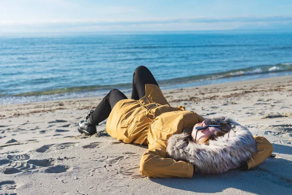 Frau mit Mantel am sonnigen Strand. — Stockfoto