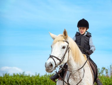 Boy riding white horse during horseback lessons. clipart
