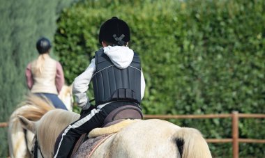 At binme dersleri sırasında beyaz ata binen çocuğun arka görüntüsü.