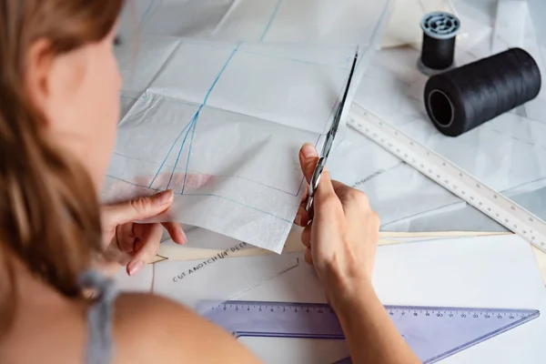 Woman tailor during work on sewing patterns, cutting pattern with scissors. Fashion design concept.