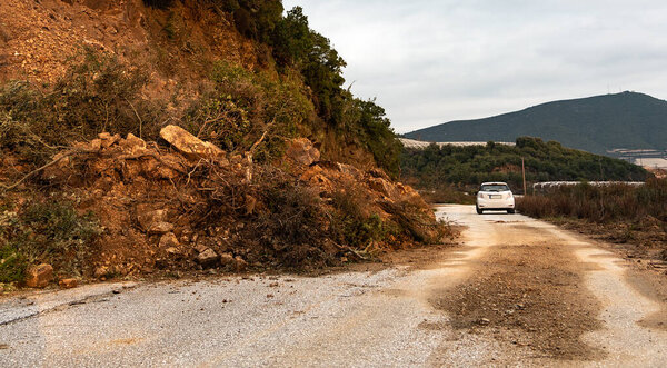 Оползень блокирует дорогу с белым хэтчбэком на заднем плане
