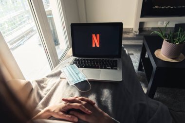 Selanik, Yunanistan - 12 Nisan 2020: Kadın karantina sırasında evinde kalırken dizüstü bilgisayarında NETFLIX izliyor. Coronavirüs salgını konsepti.