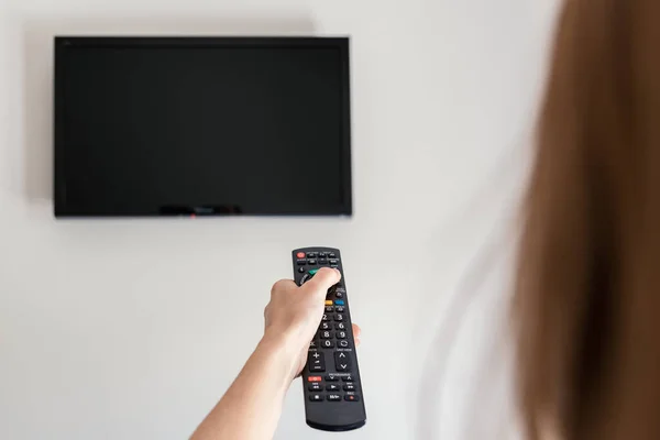 Hand holding TV remote controller to turn on TV.