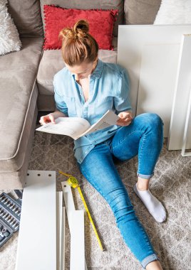 Evdeki mobilyaları monte etme talimatlarını okuyan konsantre genç bir kadın.