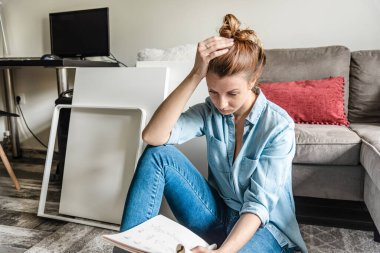 Konsantre genç bayan oturma odasında mobilyaları monte etme talimatlarını okuyor.