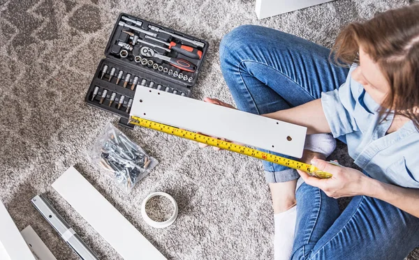 Young woman assembling new furniture for home. Woman holding yellow tape measure.