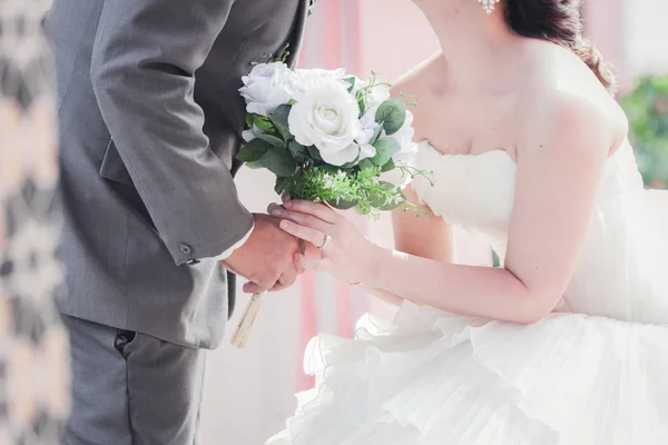 Bruid en bruidegom houden handen en een boeket van mooie bloemen — Stockfoto
