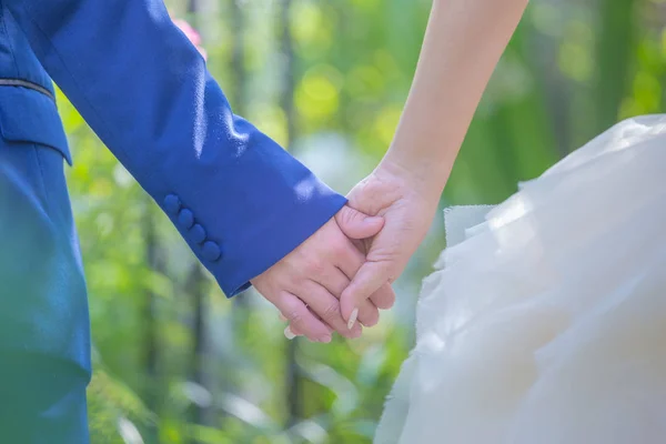 Жених держит невесту за руку на открытом воздухе свадьбы, держась за руки не — стоковое фото