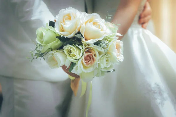 Bride and groom holding hands and a bouquet of flowers as a toke — Stock Photo, Image
