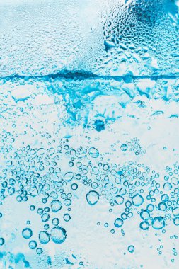 Soda ve buzun şeffaf arka planında bardağın içinde parlak mavi kabarcıklar var..