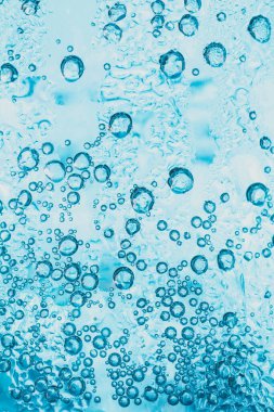 Soda ve buzun şeffaf arka planında bardağın içinde parlak mavi kabarcıklar var..