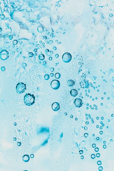 Soda ve buzun şeffaf arka planında bardağın içinde parlak mavi kabarcıklar var..