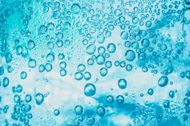 Soda ve buzun şeffaf arka planında bardağın içinde parlak mavi kabarcıklar var..