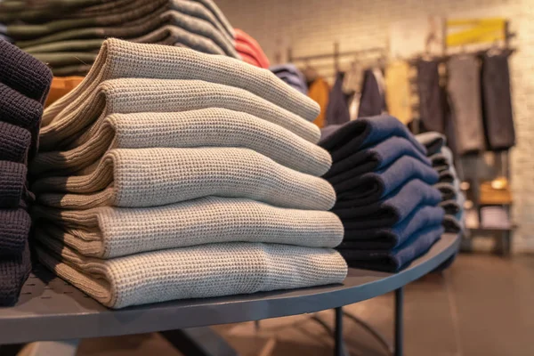 a stack of clothes in the store, pullovers and sweatshirts nicely and neatly stacked in bundles on the table, beige and gray