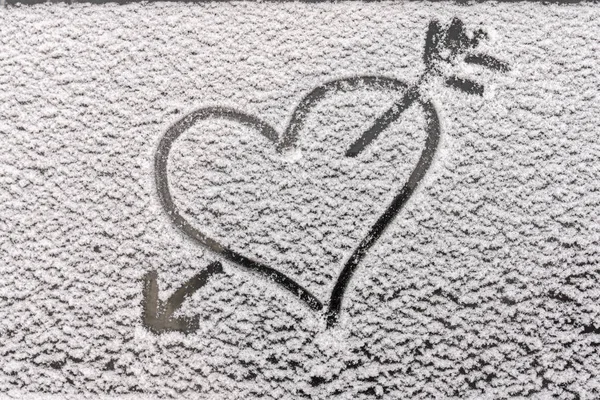 a heart and an arrow from a bow piercing it, a close-up silhouette on the snow, drawn on the glass with a finger. Romantic picture, love separation and parting and other emotions. copyspace