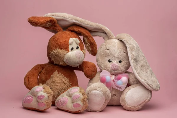 toys rabbits, a hare and a hare like a couple in love, sit next to each other. Close-up, pink background. friendship and love.