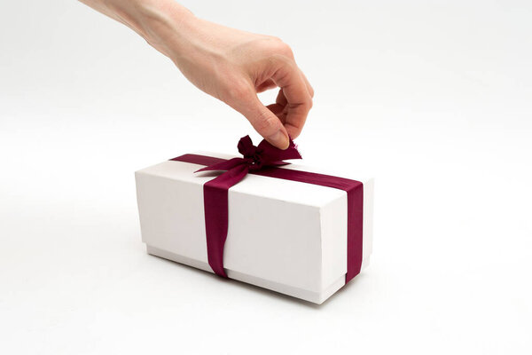 A woman's hand unties a bow on a gift box on a white background