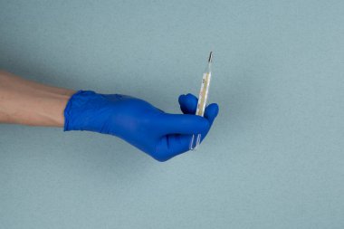 Mavi arka planda izole edilmiş eldivenli bir doktorun elindeki termometre. Coronavirus covid-19 için karantina