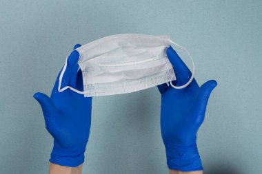 Mavi eldivenli bir doktor, hemşire ya da bilim adamının elinde gri-mavi bir arka planda izole edilmiş enfeksiyondan korunmak için tıbbi bir maske bulunur. Coronavirus covid-19 yüzünden tüm dünya karantina altında. 