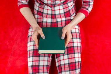 Kırmızı elbiseli bir kadın, karantina koronavirüsünde kırmızı arka planda bir kitapla süitine yerleşmiş.