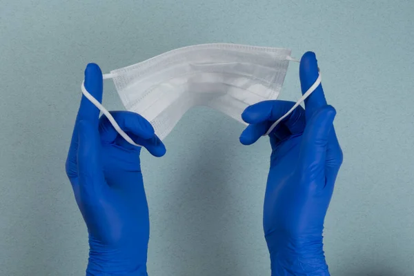 Mavi eldivenli bir doktor, hemşire ya da bilim adamının elinde gri-mavi bir arka planda izole edilmiş enfeksiyondan korunmak için tıbbi bir maske bulunur. Coronavirus covid-19 yüzünden tüm dünya karantina altında. 