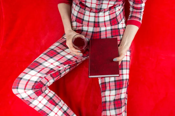 a woman in red checked home suite with a book and glass of wine at home on a red background in quarantine coronavirus covid-19, without face