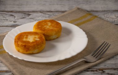 Gri keten peçetede beyaz bir tabakta peynirli kekler ve ahşap arka planda çatal.