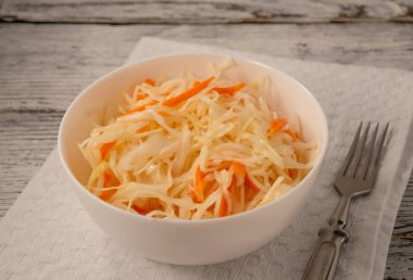 Çarşaf peçetede beyaz bir kase üzerinde lahana turşusu.