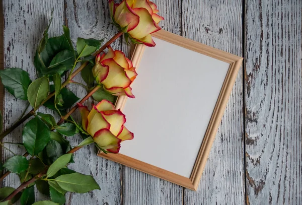 three roses on a wooden background with a white leaf in the frame for the inspiration, top view