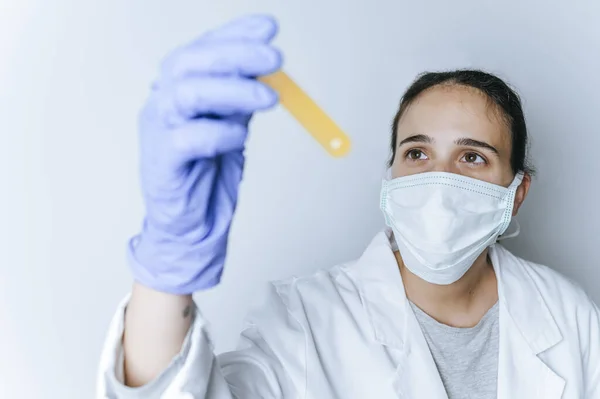 Female doctor with mask looking at test tube