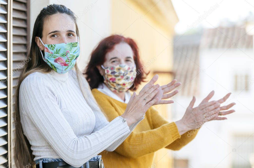Two women with face mask clapping on the balcony