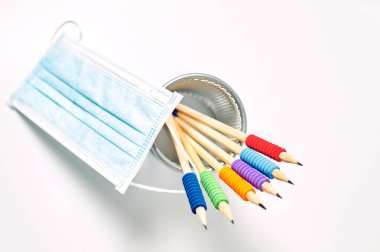 Beyaz arkaplanda renkli kalem ve antiviral maske