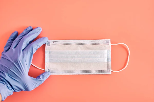 Hand holding antiviral mask on pink background