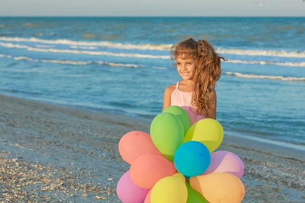 Glückliches kleines Mädchen am Strand mit Luftballons. — Stockfoto