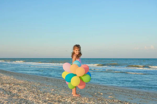 Glückliches kleines Mädchen am Strand mit Luftballons. — Stockfoto