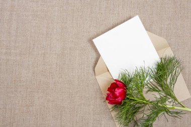 Bej kumaş üzerine bir zarf ve kırmızı çiçekli kart. 