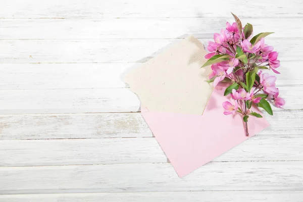 Tarjeta con sobre rosa y flores rosas de manzano sobre tabla de madera . —  Fotos de Stock