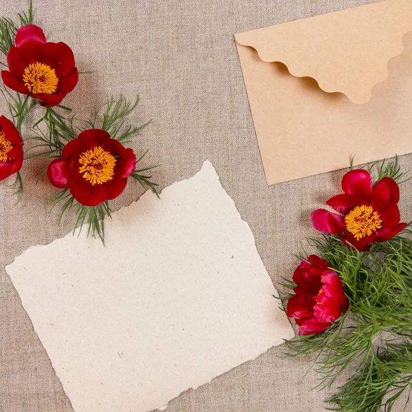 Tarjeta con sobre y flores rojas sobre tela beige . —  Fotos de Stock
