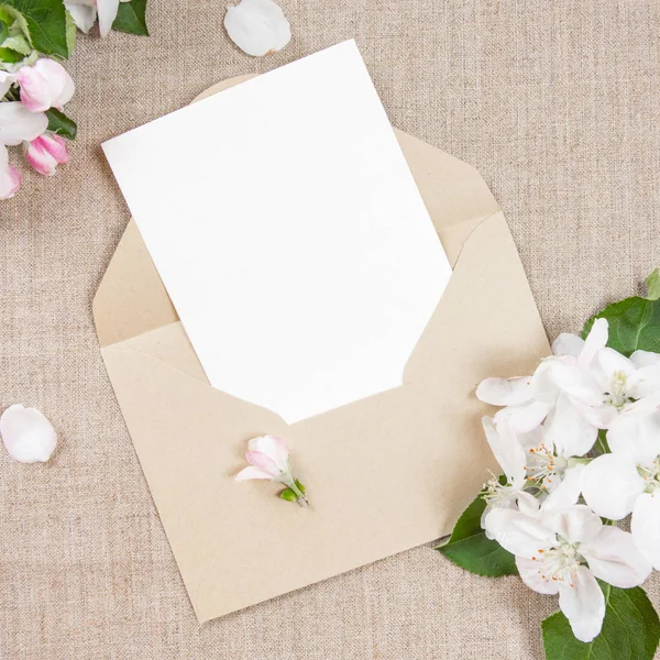 Card with an beige envelope and white flowers of apple tree on beige fabric. — Stock Photo, Image