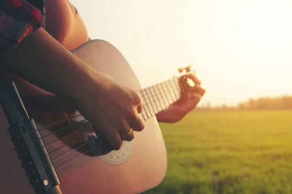 女性の手を閉じて太陽の光で草原でギターを弾く — ストック写真